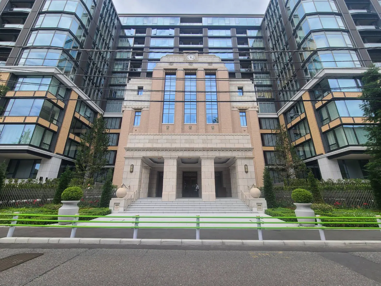 - モダンな高層マンションとクラシックなデザインのエントランス、整備された植栽とシンプルな階段が特徴の建物外観
