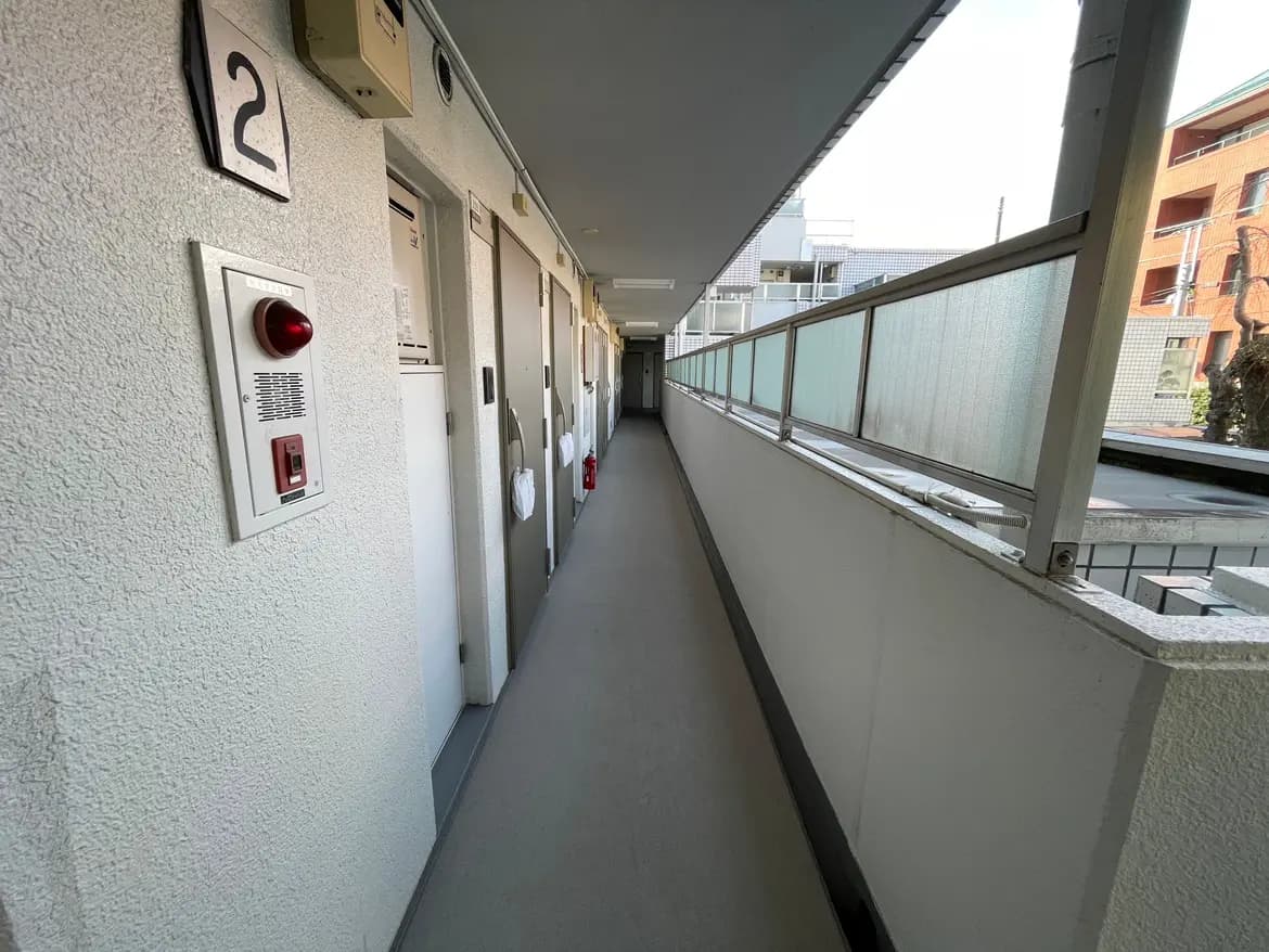 - 2号室の表示があるマンションの廊下、手すりと防火器具、真っ直ぐに続く扉が見えるインテリア景観