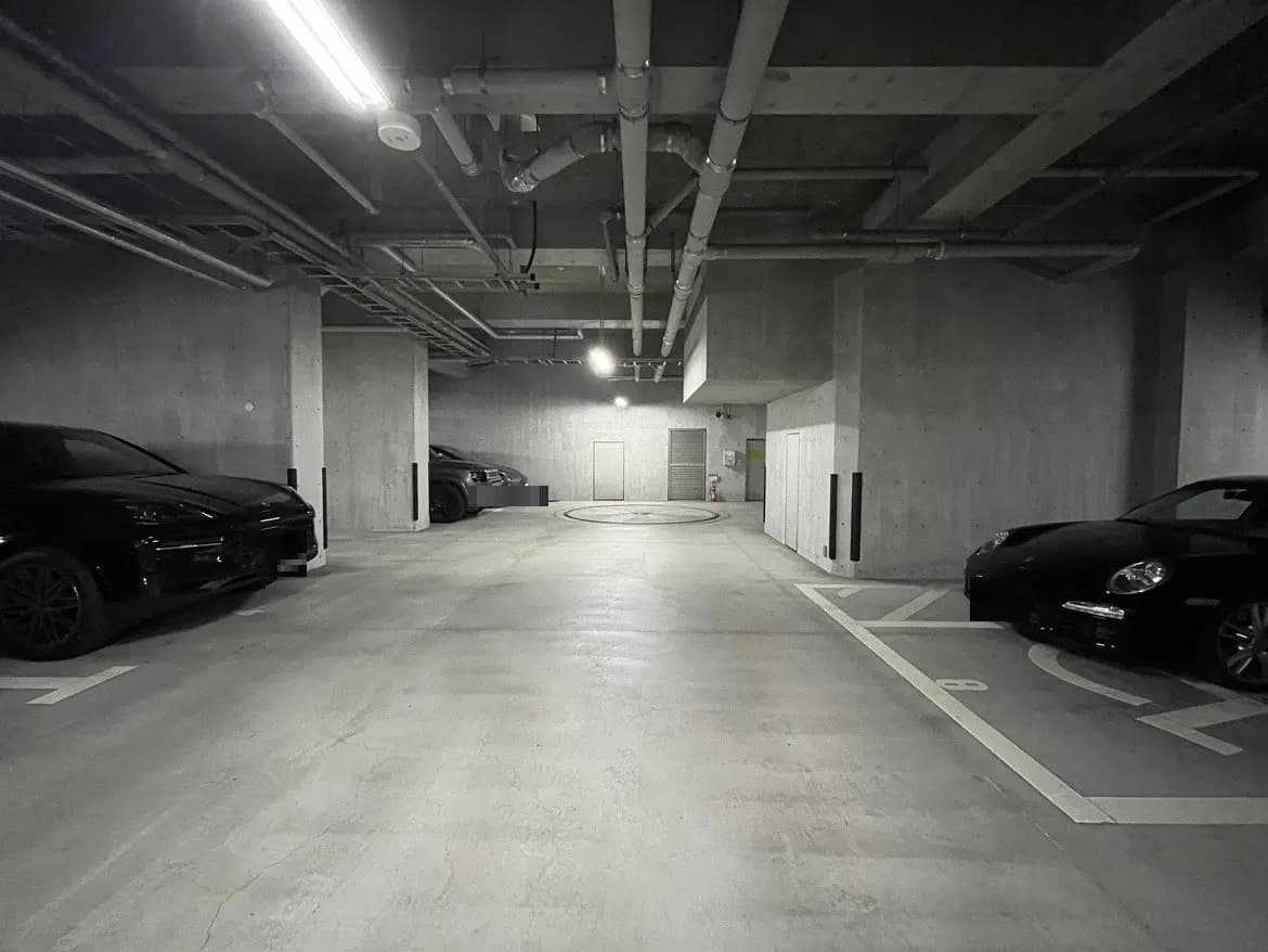 - 明るい照明が設置されたモダンなコンクリート製の駐車場、黒い車が数台駐車されている様子