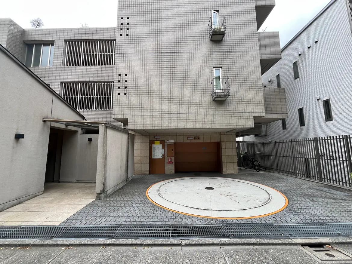 - モダンな建物のエントランス、丸い車寄せと木製の扉、隣接する駐輪スペースのある外観