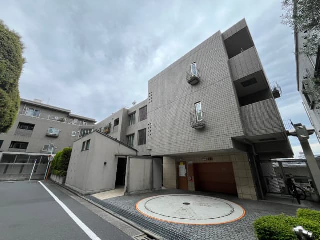 - グレーのタイル張りの住宅ビル、バルコニーが付いた外観、周囲の緑と舗装された駐車スペースが特徴的なエリア