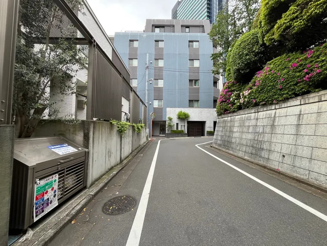 - 都市の住宅地にある狭い道路と巧妙に配置された緑の植栽、周囲の高層ビルが見える街の風景