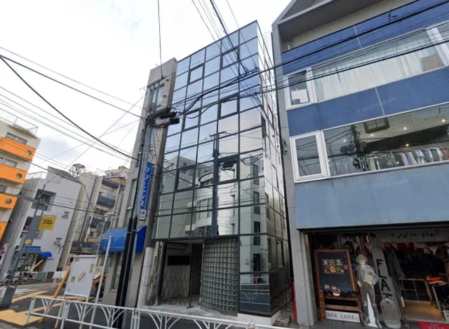 - モダンなガラス張りのビルと隣接する店舗、周囲に電線が見える都市の風景