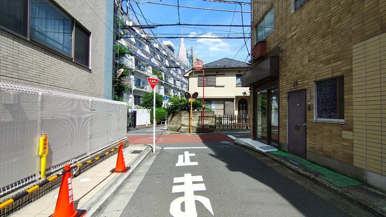 - 道路の分岐点、赤信号と停止標識がある交差点、周囲には住宅と電線が見える街並みの風景
