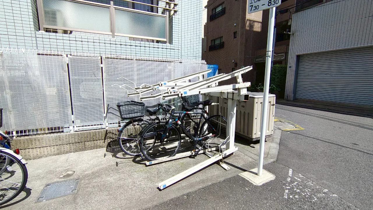 - 自転車ラックに停められた自転車とメッシュフェンス、周囲のビルが映る街角の風景