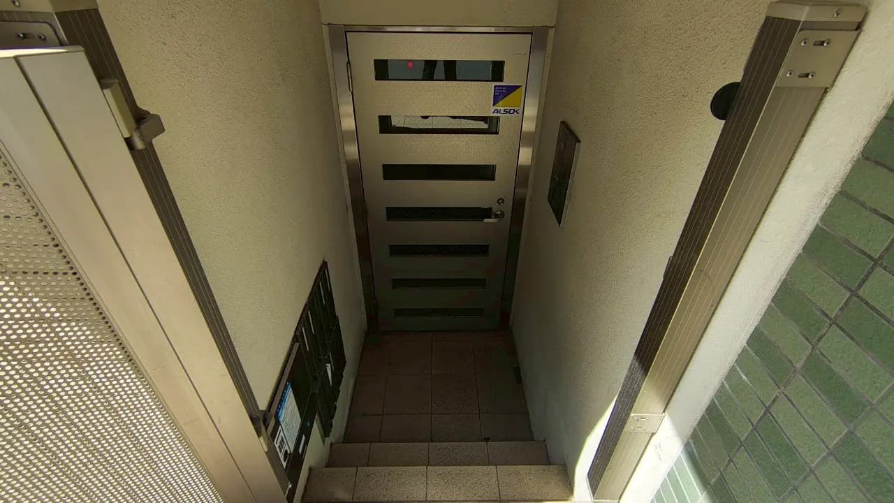 - 階段を下りた先にあるモダンなデザインの入口ドア、隣には郵便受けが設置されたアプローチの風景