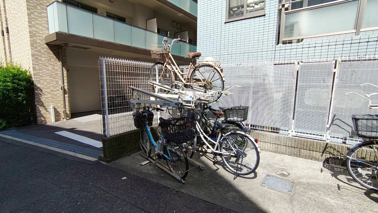 - アパートメントの駐輪場に置かれた自転車、上段に積まれた白い自転車と手前の青い自転車、おしゃれなデザインの自転車が並ぶ風景