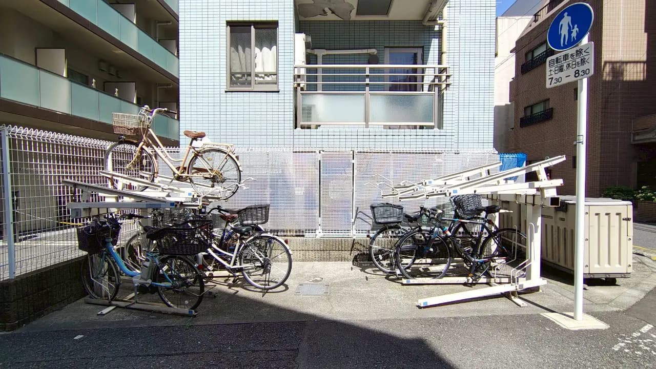 - アパートの自転車置き場、上下二段の自転車ラックに自転車が停められている様子、周囲のマンションと日差しの入る明るい環境