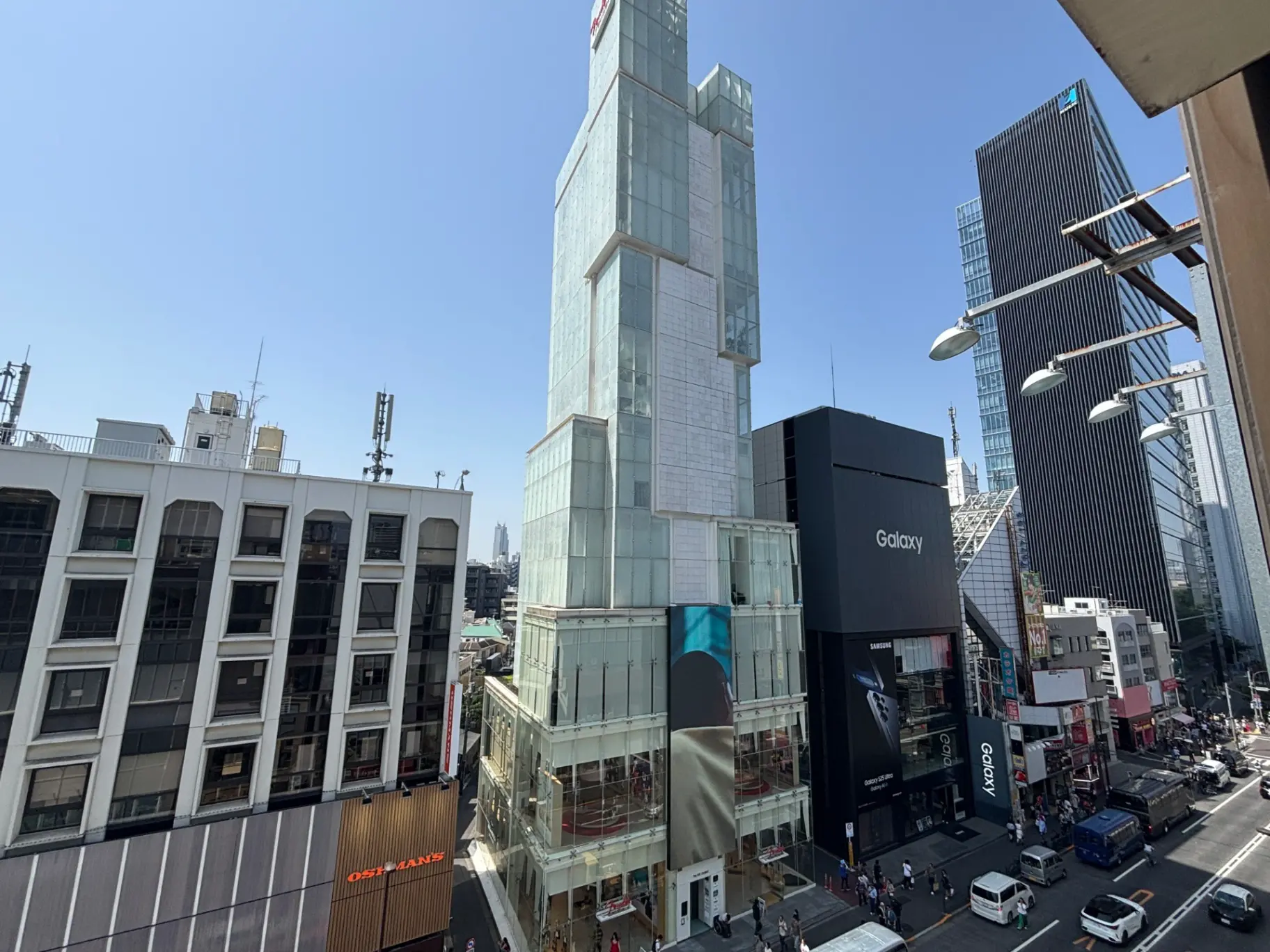 - 青空の下に立つ現代的なビル群、手前には「Galaxy」の看板が見える繁華街の風景