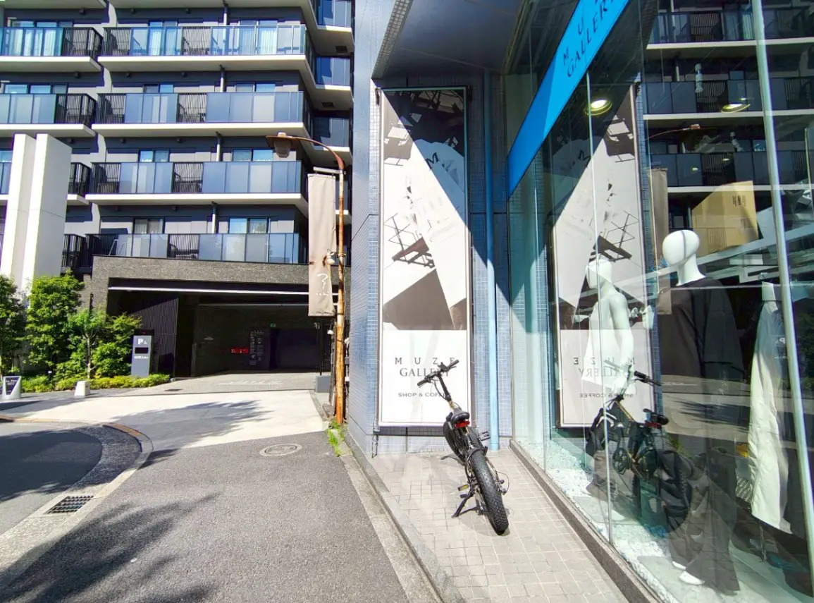 - 都市のギャラリーの前に停まった電動自転車、近くのマンションと洗練されたショーウィンドウのディスプレイが見える風景