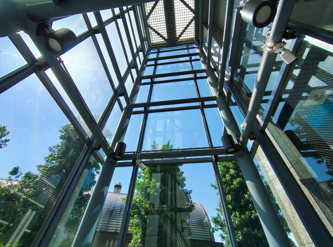 - ガラス張りの天井から青空が見える現代的な建物の内部、金属製のフレームと照明器具が印象的なデザイン