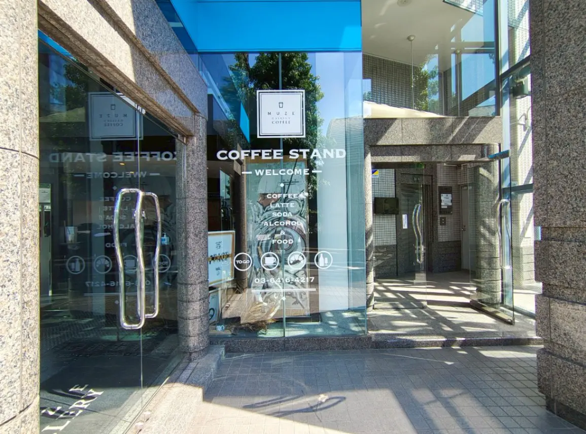 - モダンなコーヒースタンドのエントランス、ガラスの扉とウィンドウに表示されたメニュー、日差しが差し込む明るい雰囲気の外観