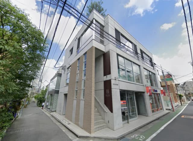 - コンクリートとガラスを使ったモダンな外観のビル、周囲には緑と静かな街並みが広がる景観