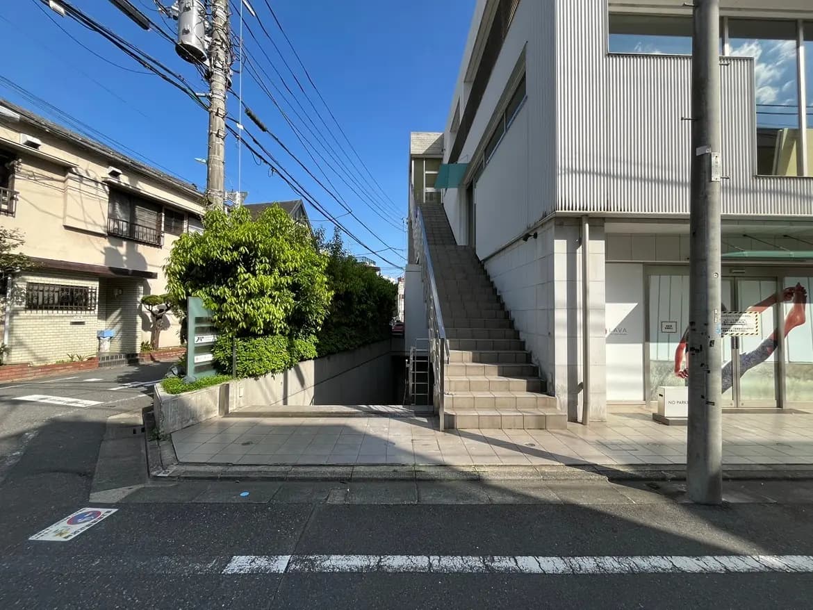 - 現代的なビルの外観、白い外壁と階段、近くにある住宅街の景観と青空が広がる様子