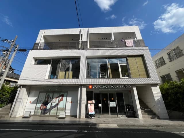 - モダンな外観のホットヨガスタジオ「LAVA」、大きなガラス窓と洗練されたデザインが特徴的な建物と青空