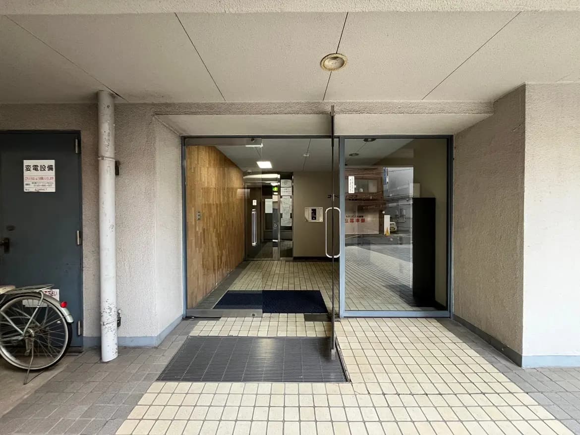 - 入口のガラスドアと木材の壁が特徴的なマンションのエントランス、左側には自転車が置かれている様子