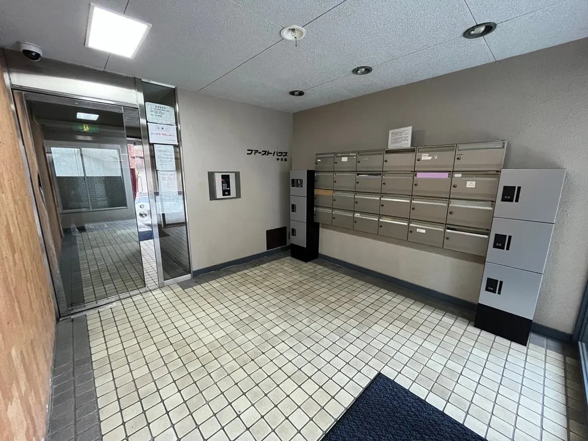 - モダンなマンションのエントランス、郵便受けとロッカーを備えたシンプルな内装、明るい照明とセキュリティカメラが設置された空間
