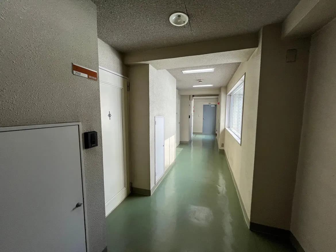 - 明るい色調のマンションの廊下、両側に部屋のドアと窓、整った清掃状態のフロアマットなフロアデザイン