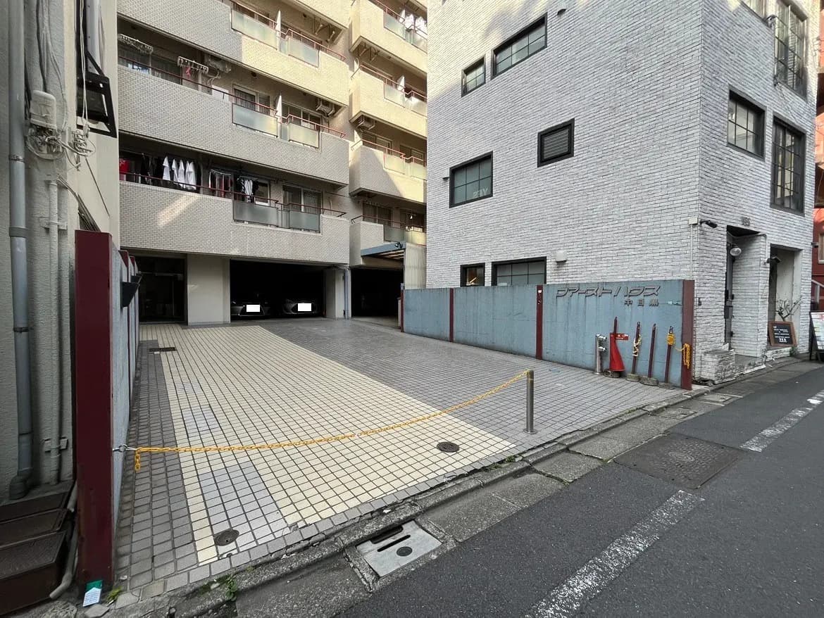 - 都市部のアパートメントエリア、コンクリートブロックの壁とタイル敷きの駐車場、洗濯物が干されたバルコニー付きの建物