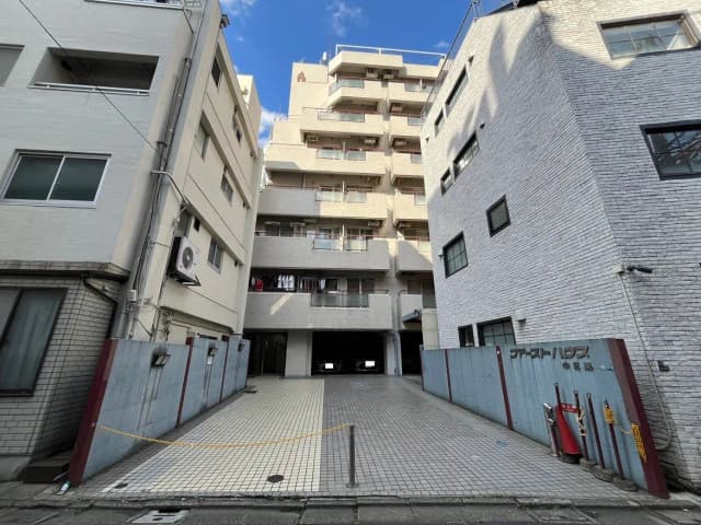 - 市街地に位置するアパートの外観、駐車場と建物、青空が広がる日の光が差し込む風景