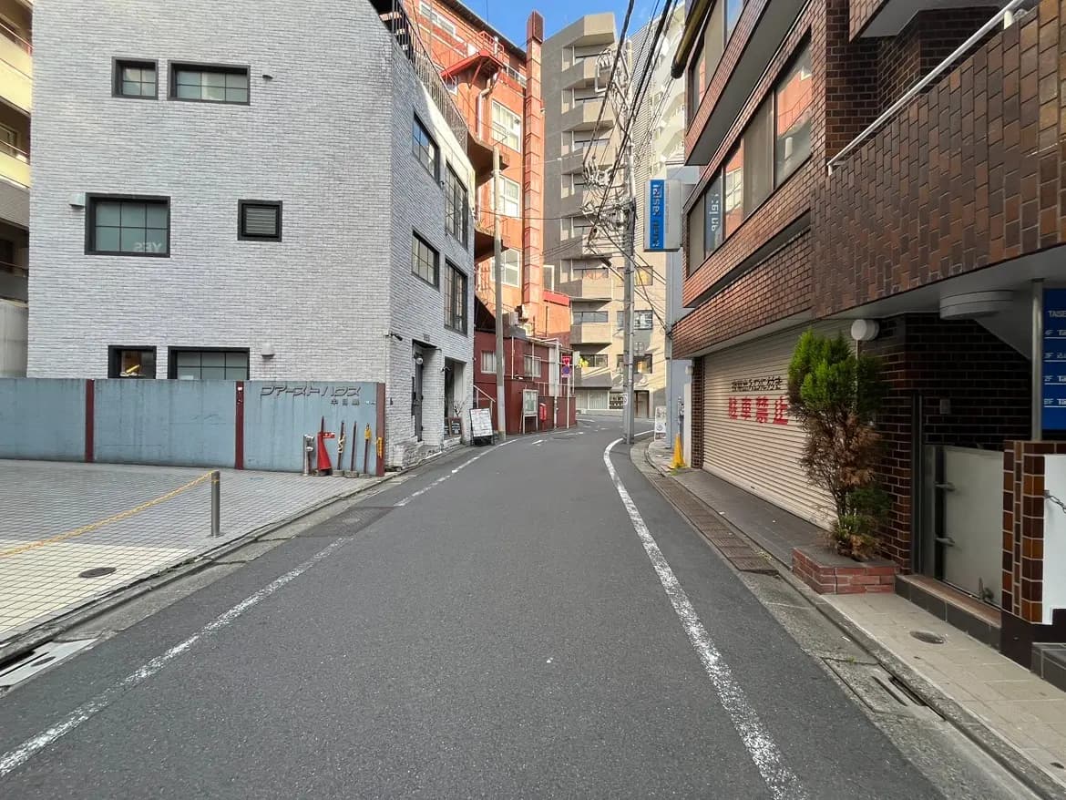 - 都市の中の狭い通り、レンガ造りの建物と白い外壁の建物が並ぶ風景、青空が広がる昼間の風景
