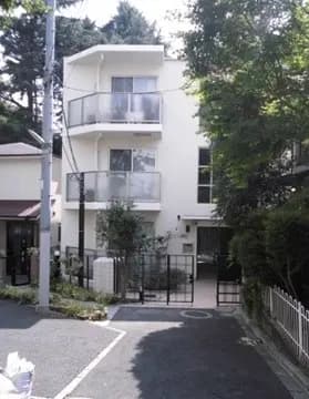 - 清潔感のある白い外壁の三階建てアパート、バルコニー付きで周囲には緑豊かな植栽が施されている住宅の外観