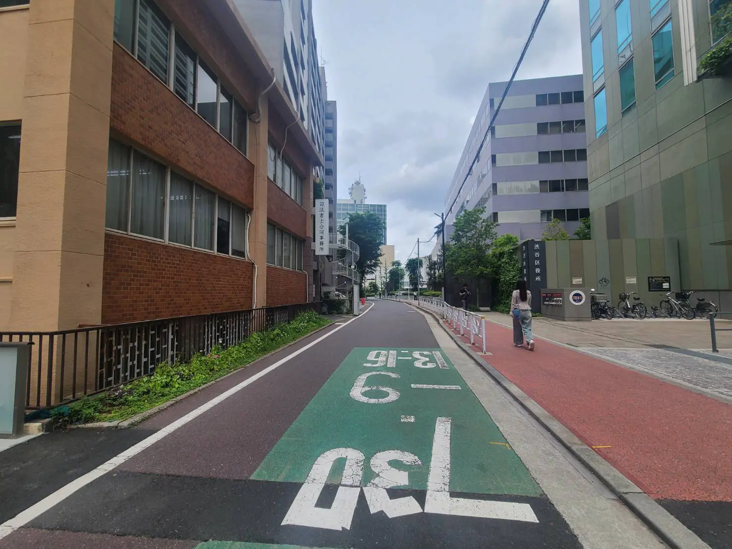 - 緑色の自転車専用道路と退廃的な通りを歩く女性、両脇に高層ビルが立ち並ぶ都市風景
