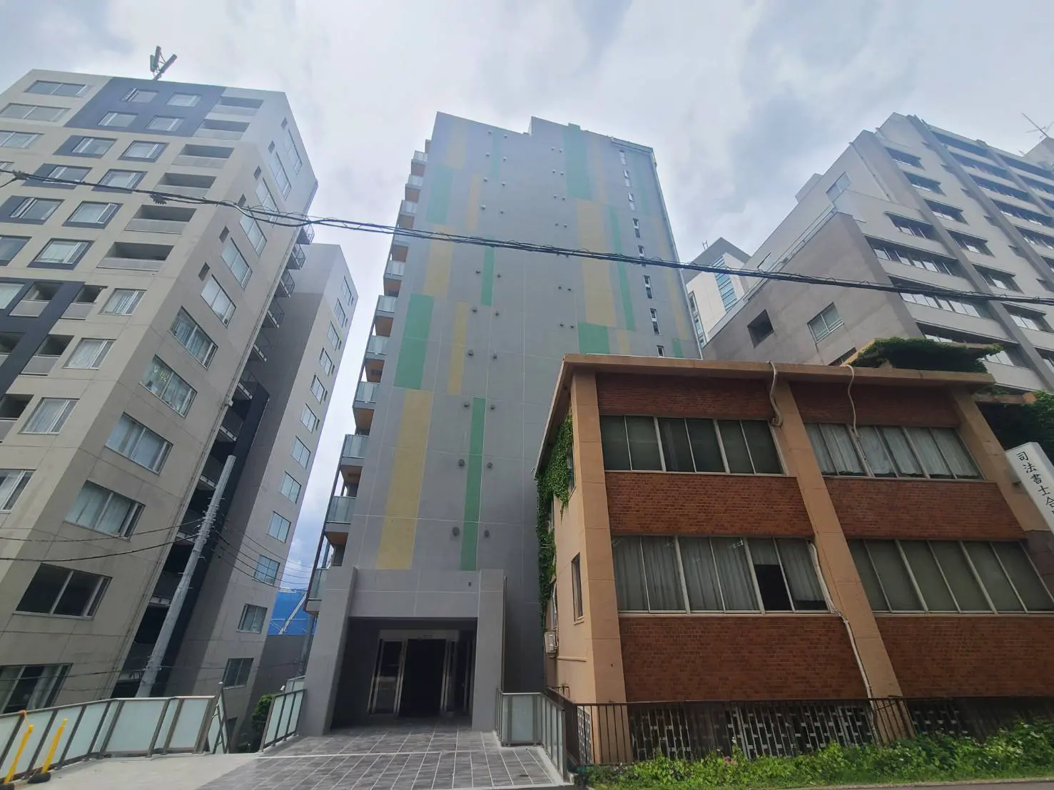 - モダンなデザインの高層マンション、新旧の建物が隣接する都心の風景、曇り空の下での外観全景