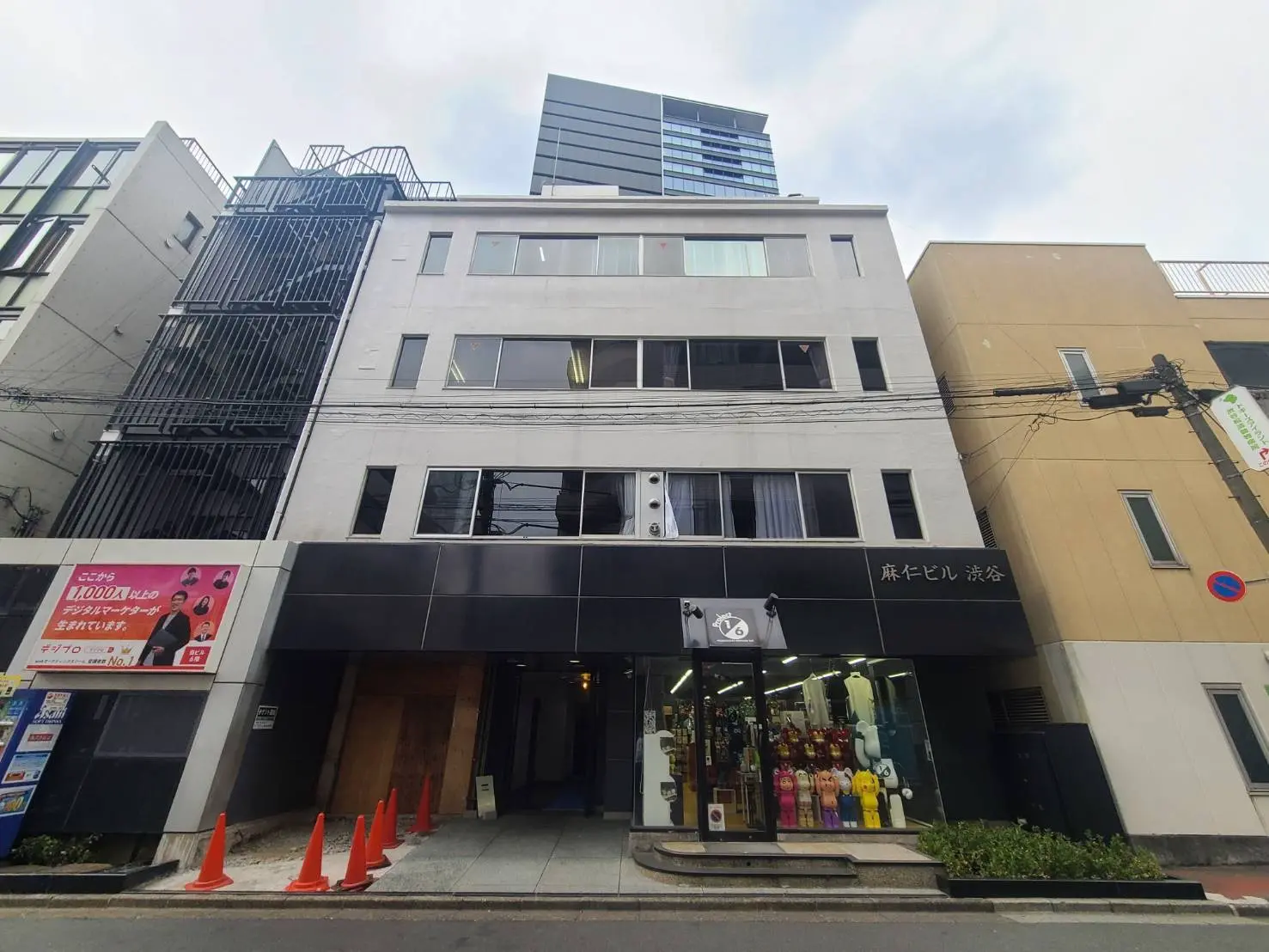 - 渋谷にある麻仁ビルの外観、黒いファサードと透明なガラス、周囲に立つ高層ビルと交通標識が見える街並み