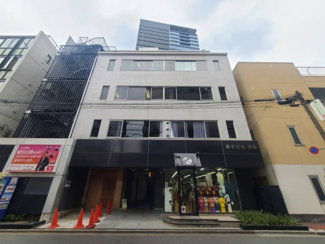 - 渋谷にある麻仁ビルの外観、黒いファサードと透明なガラス、周囲に立つ高層ビルと交通標識が見える街並み