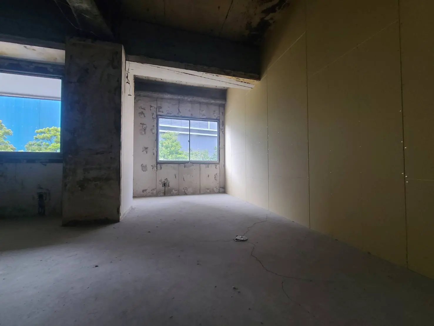 - 未完成の部屋、コンクリートの床とむき出しの壁、外の緑が見える窓からの自然光が差し込む様子