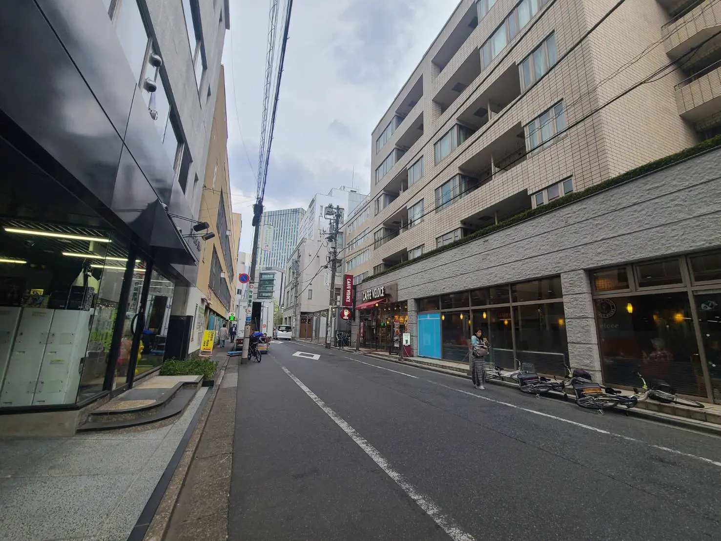 - 都会的な街並み、アパートメントビルとカフェ、歩道に置かれた自転車と人々が行き交う風景