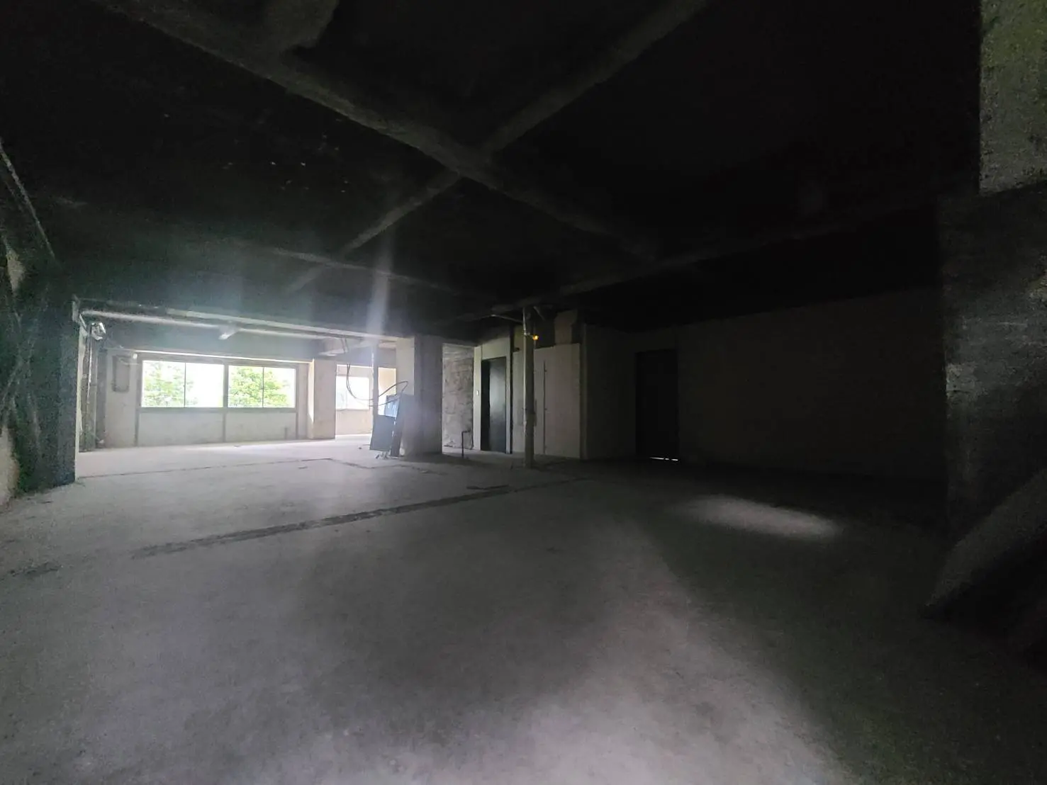 - 明るい自然光が差し込む広々とした空間、未仕上げのコンクリートの床と天井が特徴的な室内写真