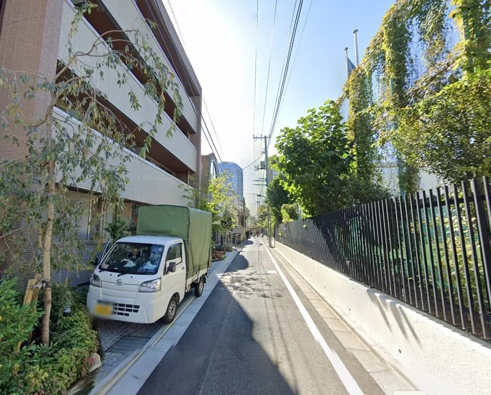 - 緑豊かな街並みの脇に停車している軽トラック、周囲にはマンションや青空が広がる風景