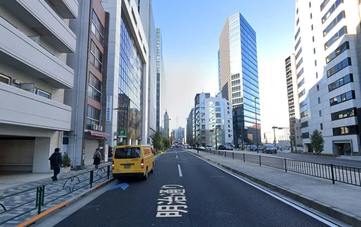 - 高層ビルが立ち並ぶ都市の街並み、左側には白いマンションと黄色いバン、右側にはガラス張りのオフィスビルが映る風景