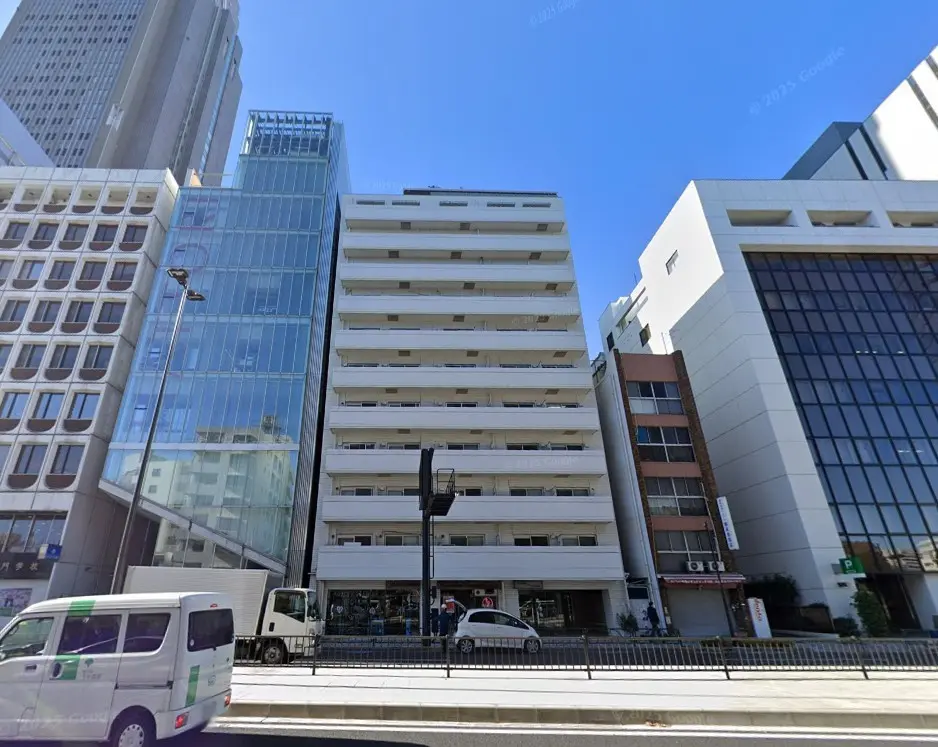 - 近代的な高層ビルと商業ビルが立ち並ぶ、都心の街並みを背景にした白いマンションの外観