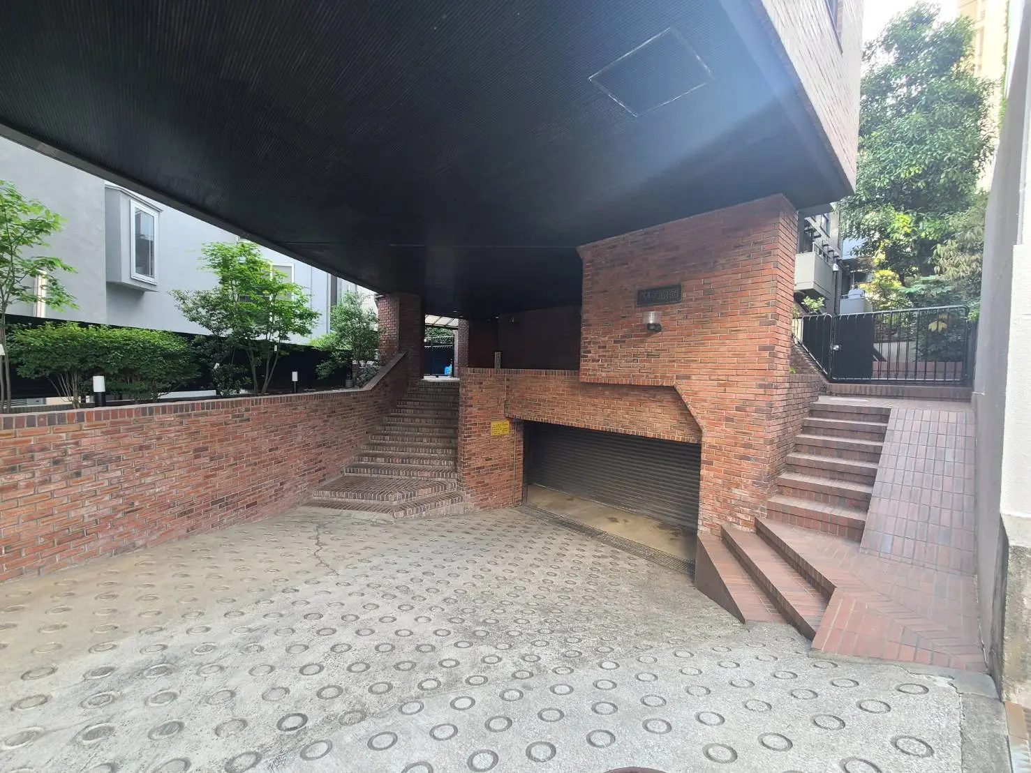 - レンガ造りのアプローチと階段が特徴的な建物のエントランス、緑豊かな植栽とシャドーが美しいスペース