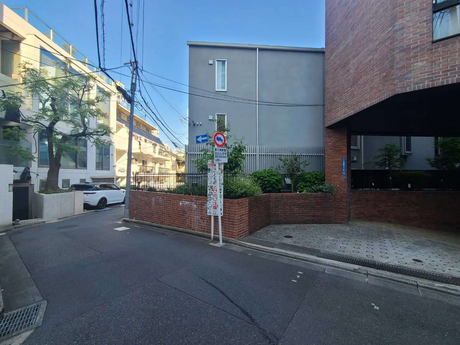 - 都市の風景にある交差点、近代的な建物と植栽が配置された街路、白い車と標識が見えるシーン