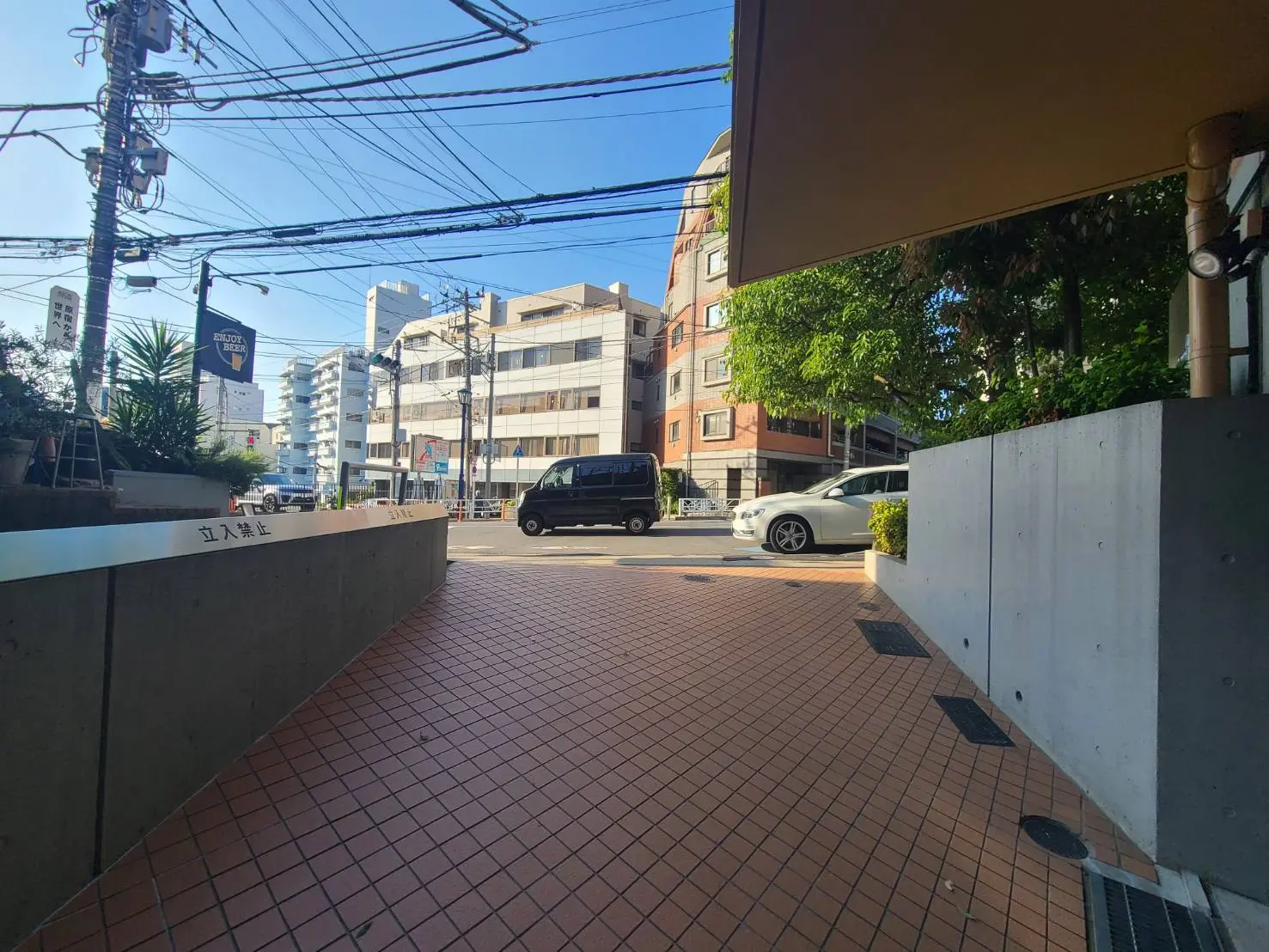 - 都市の歩道の風景、整備されたタイルの道と建物の並ぶ通り、電線が交差する青空の下の街並み