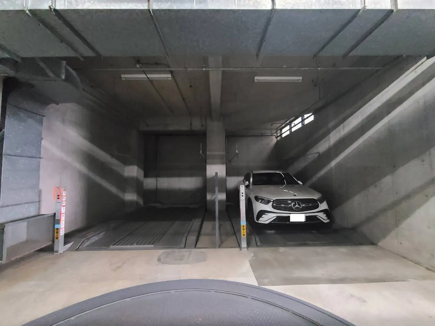 - 近未来的な車両用駐車スペース、コンクリートの壁に囲まれたリフト式の駐車システムが特徴、白い高級車が停まっているガレージ内部の画像