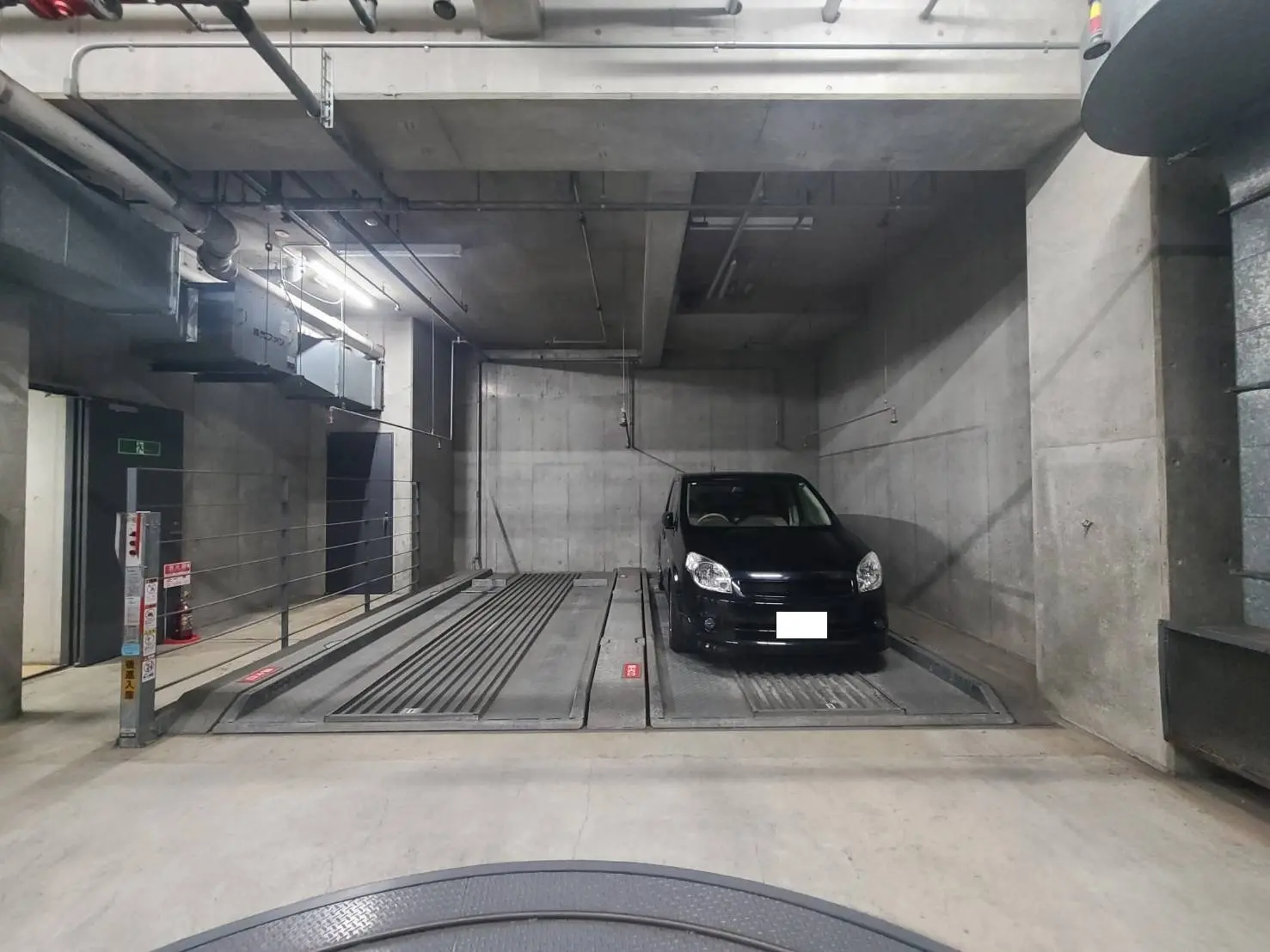 - モダンな駐車場の内部、コンクリート壁、車両昇降機に停められた黒い車の様子