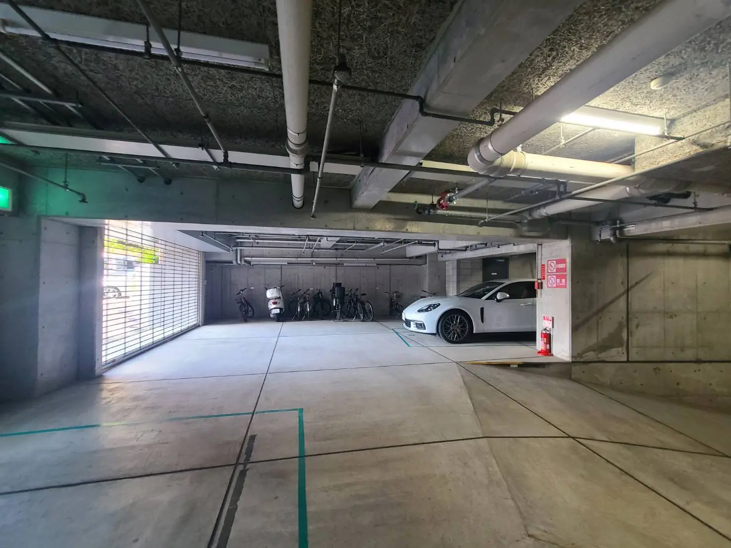 - コンクリート製の駐車場、白いスポーツカーと自転車が並ぶ車両置き場の様子、明るい照明と開放感のあるデザイン