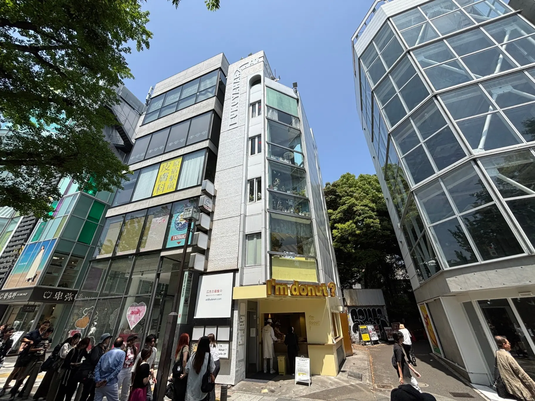- 明るい青空の下、ガラスの外観を持つモダンな建物と行列の人々が見える街の風景