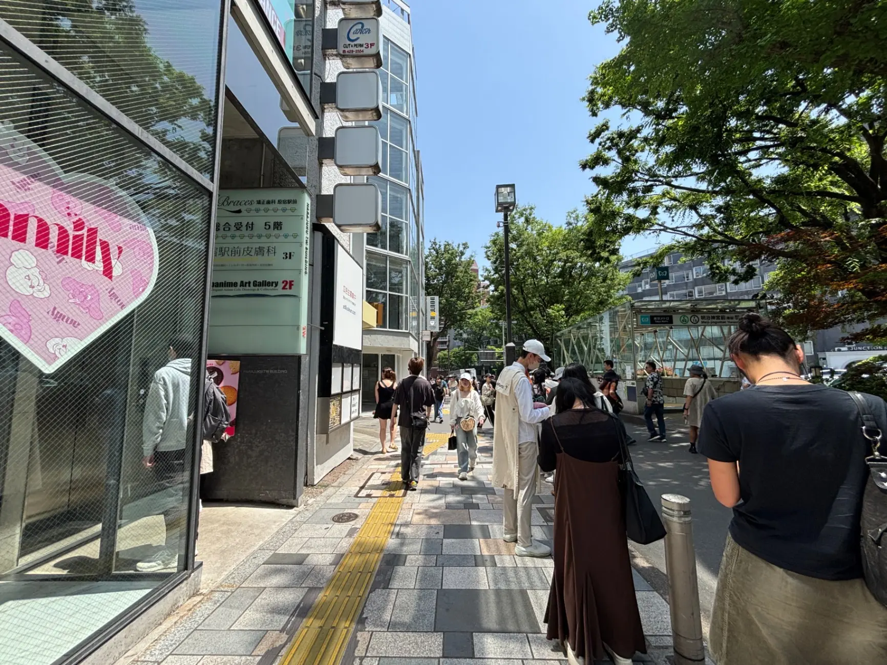 - 活気ある繁華街の風景、多くの人々が行き交い、緑豊かな木々が並ぶ通り、とアートギャラリーの看板が見える景色