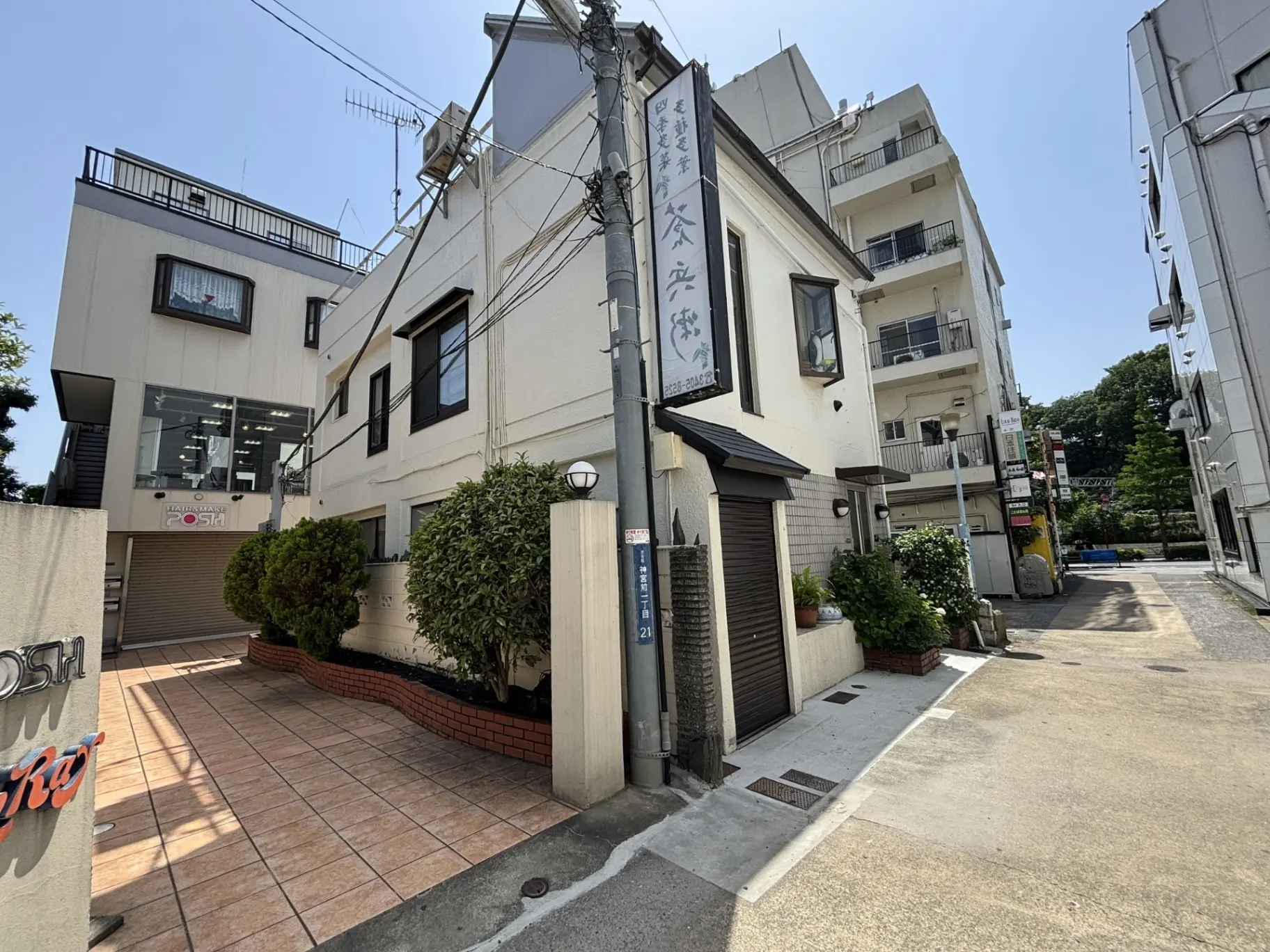 - 白い外壁の建物と広々とした舗装されたエントランス、周囲に緑が配された商業施設の入口の風景