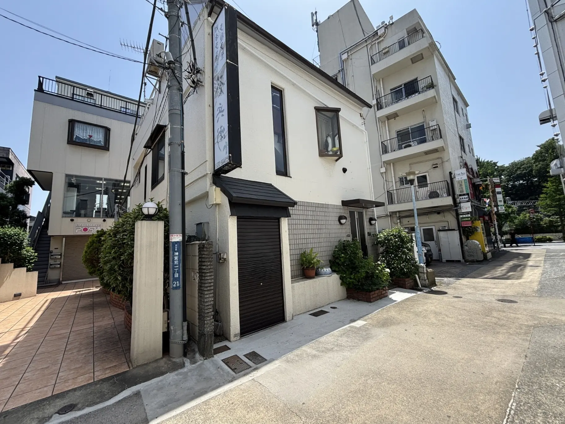 - 住宅街の一角にある白い外壁の建物、隣に高層ビルが立ち並ぶ様子、青空の下での風景