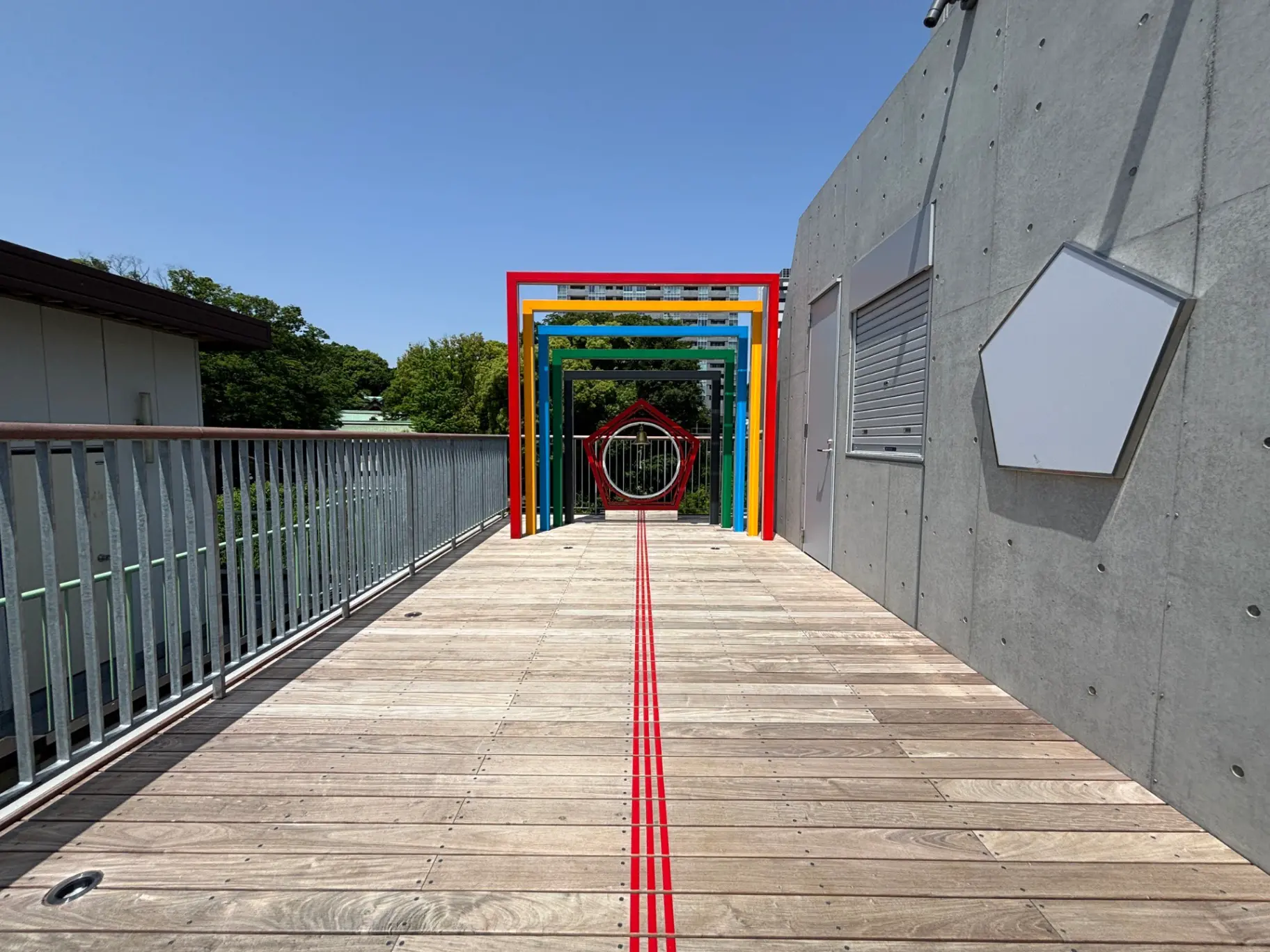 - カラフルなアーチ型のオブジェが並ぶ明るいバルコニー、木製の床と青空が広がる風景