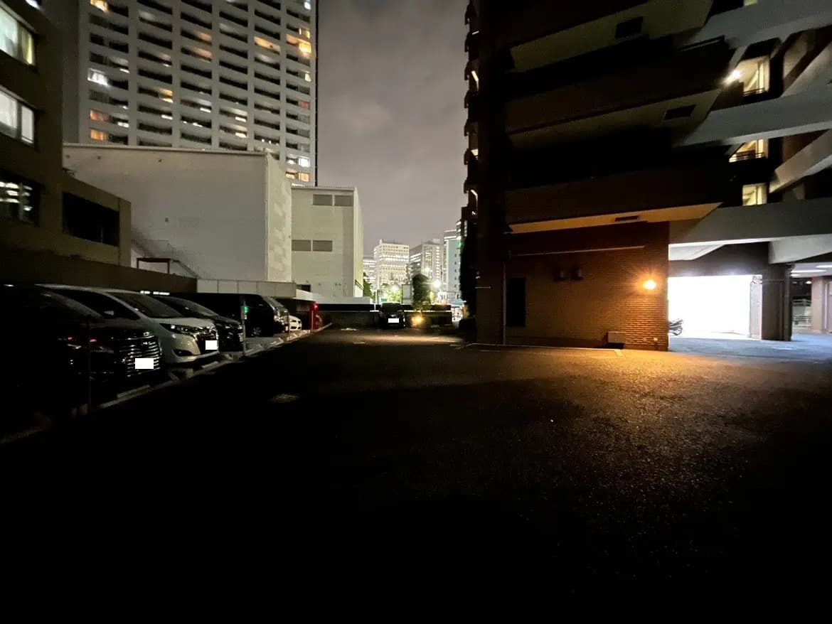 - 夜の都市風景、暗い駐車場と周囲のビル、遠くに明かりが灯る高層ビルのシルエット