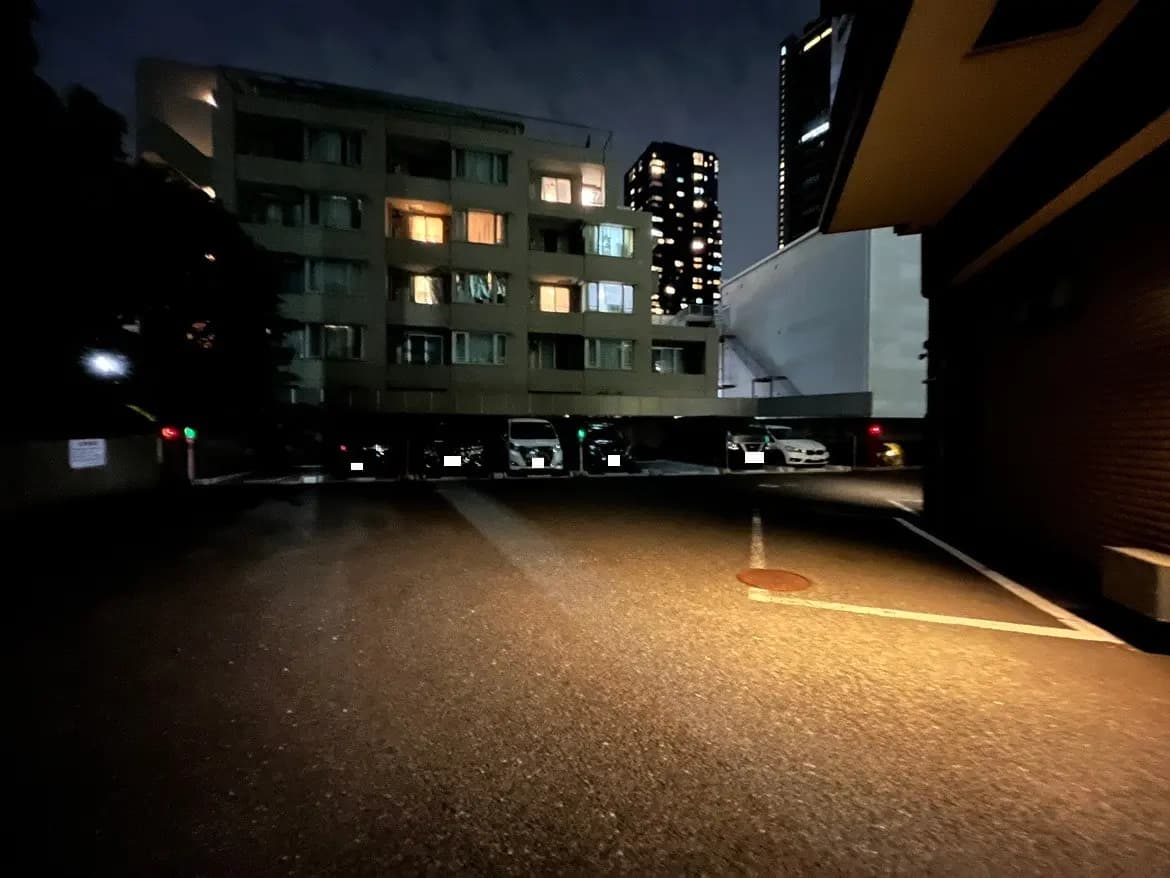- 夜の都市風景、マンションの明かりが灯り、駐車場に停まった車が見える暗い路地の画像