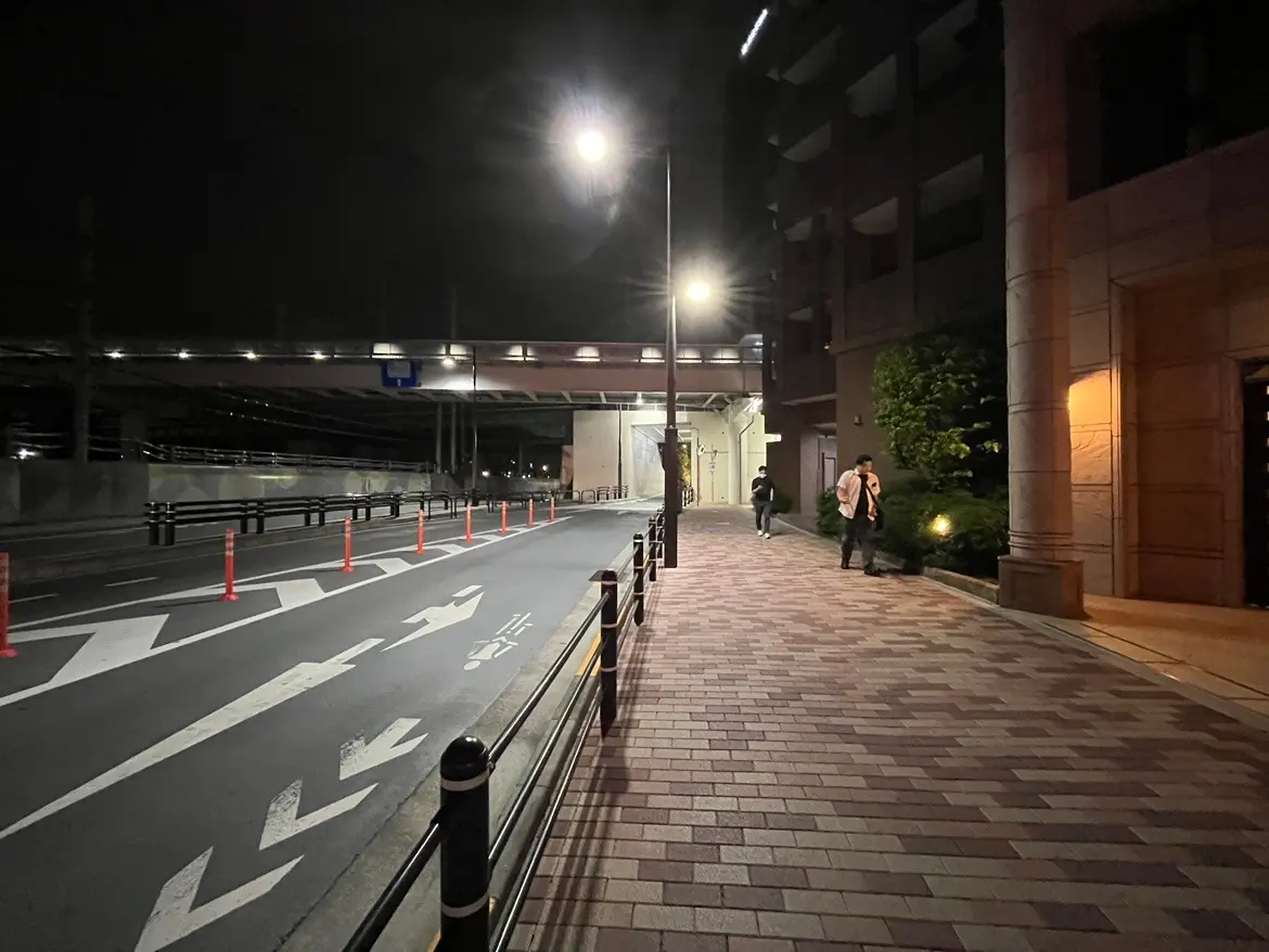 - 夜景の都市風景、街灯に照らされた歩道と交通標識、通行中の人々が見える風景
